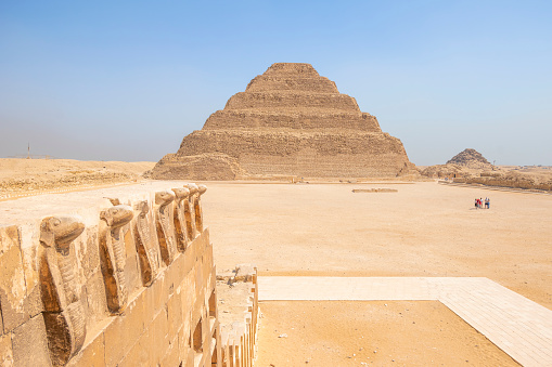 The Step Pyramid, Sakkara, Egypt - July 26, 2022: Saqqara, also spelled Sakkara or Saccara in English is an Egyptian village in Giza Governorate, that contains ancient burial grounds of Egyptian royalty, serving as the necropolis for the ancient Egyptian capital, Memphis. \nSaqqara contains numerous pyramids, including the Step Pyramid of Djoser, sometimes referred to as the Step Tomb, and a number of mastaba tombs. Located some 30 km (19 mi) south of modern-day Cairo, Saqqara covers an area of around 7 by 1.5 km (4.3 by 0.9 mi).\n\nSaqqara contains the oldest complete stone building complex known in history, the Step Pyramid of Djoser, built during the Third Dynasty. Another sixteen Egyptian kings built pyramids at Saqqara, which are now in various states of preservation. High officials added private funeral monuments to this necropolis during the entire Pharaonic period. It remained an important complex for non-royal burials and cult ceremonies for more than 3,000 years, well into Ptolemaic and Roman times.