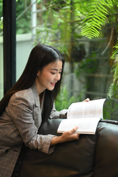 istock Beautiful millennial woman reading book while resting on couch at her office. 1419830378