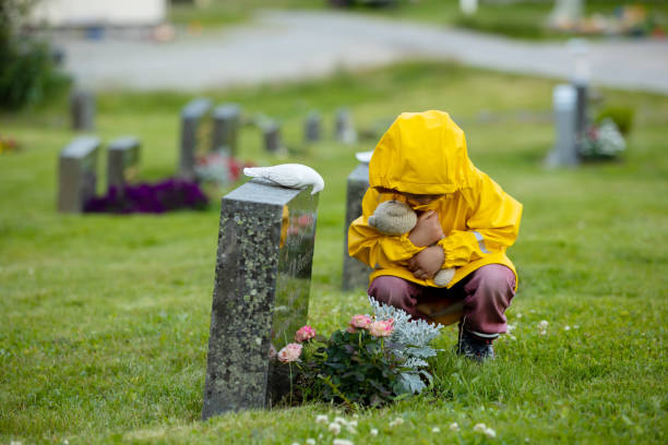 sad little child, blond boy, standing in rain on cemetery, sad person, mourning - cemetery child mourner death imagens e fotografias de stock