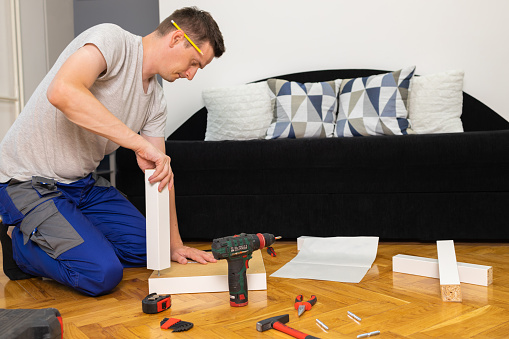 The young man assembles the wooden leg of the table