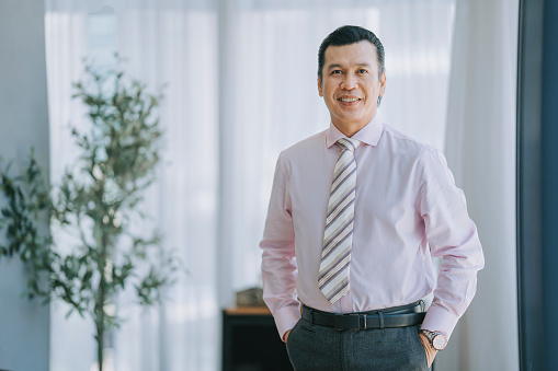 asian malay bank manager looking at camera smiling in office standing beside window
