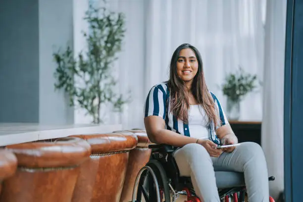 Asian indian woman with disabilities sitting on wheelchair looking at camera smiling in meeting room