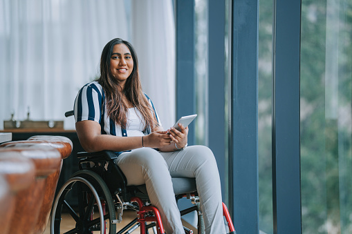 Asian indian woman with disabilities sitting on wheelchair looking at camera smiling in meeting room