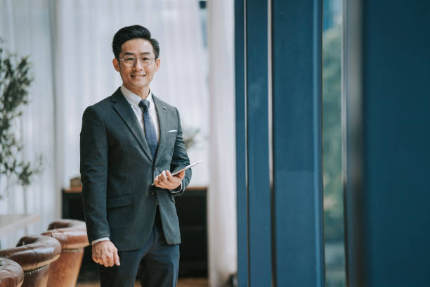 Asian Chinese Businessman looking at camera smiling standing in front of window in conference room stock photo