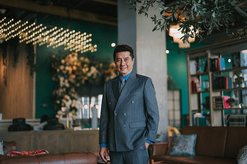 Portrait Asian Chinese successful businessman looking at camera smiling standing at luxury hotel lobby