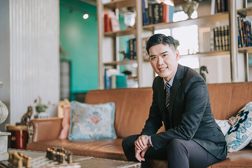 Portrait Asian Chinese successful businessman looking at camera smiling at living room sitting on sofa