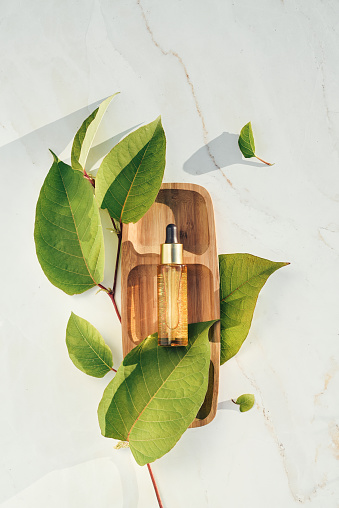 Natural serum golden with colloidal gold with leaves on a wooden tray, podium. Natural beauty and skin care product concept. Top view, flat lay