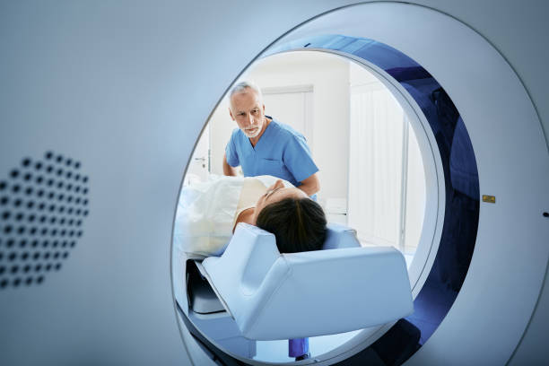 ct scan technologist overlooking patient in computed tomography scanner during preparation for procedure. woman patient going into ct scanner - radiologist imagens e fotografias de stock