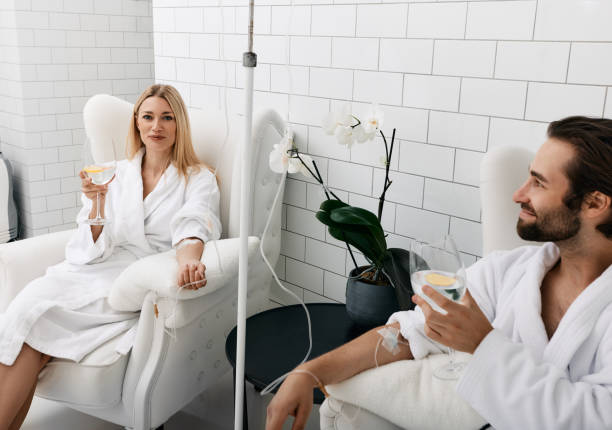 pareja enamorada durante la terapia vitamínica intravenosa. hermosa mujer con su novio con vasos de bebida refrescante con limón en clínica médica para desintoxicar sus organismos - spa treatment health spa couple happiness fotografías e imágenes de stock