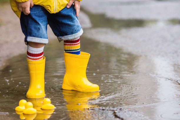 istock A small child in rainbow socks, yellow rubber boots and a jacket runs through puddles, has fun and plays after the rain. A picture of summer and autumn holidays. Legs close-up. 1419846664