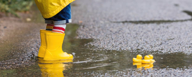 istock A small child in rainbow socks, yellow rubber boots and a jacket runs through puddles, has fun and plays after the rain. A picture of summer and autumn holidays. Legs close-up. 1419846675