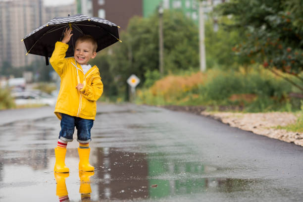istock A small child in rainbow socks, yellow rubber boots and a jacket runs through puddles, has fun and plays after the rain. A picture of summer and autumn holidays. A child under an umbrella. 1419846783