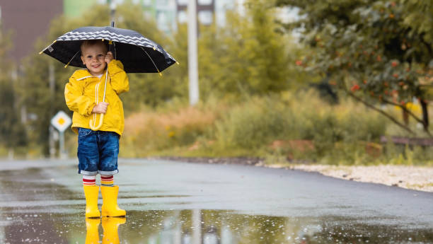 istock A small child in rainbow socks, yellow rubber boots and a jacket runs through puddles, has fun and plays after the rain. A picture of summer and autumn holidays. A child under an umbrella. 1419846794