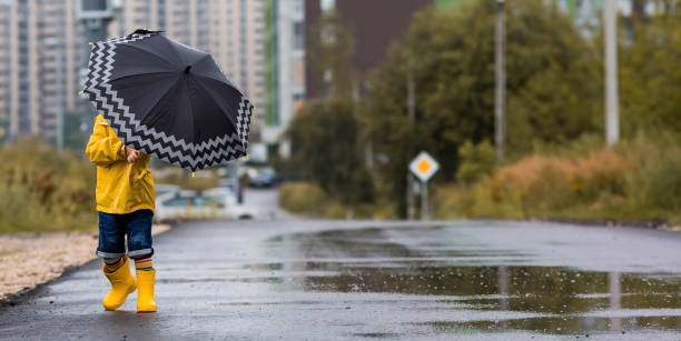 istock A small child in rainbow socks, yellow rubber boots and a jacket runs through puddles, has fun and plays after the rain. A picture of summer and autumn holidays. A child under an umbrella. 1419846805