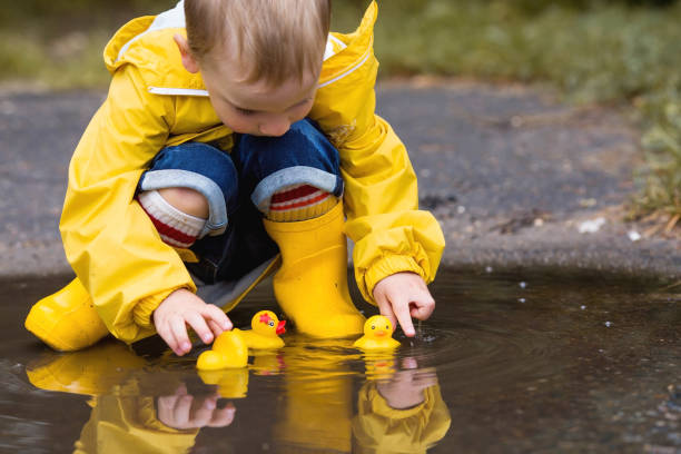 istock A small child in rainbow socks, yellow rubber boots and a jacket jumps through puddles and plays with yellow rubber ducks. A picture of summer and autumn holidays. A child in the rain. 1419846832
