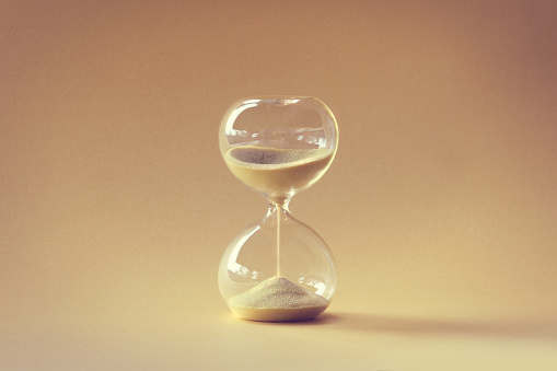Hourglass, also known as sandglass, sand timer, sand clock. Single yellow object on earth colored beige orange paper. Monochromatic background image.
