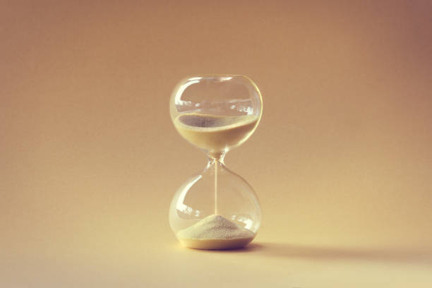 Hourglass, passage of time from 2022 to 2023 year. Wood artistic model hand holding time glass. Countdown to winter holidays. Merry Christmas and a Happy New Year. Yellow orange monochromatic image.. Hourglass, also known as sandglass, sand timer, sand clock. Single yellow object on earth colored beige orange paper. Monochromatic background image. hourglass stock pictures, royalty-free photos & images