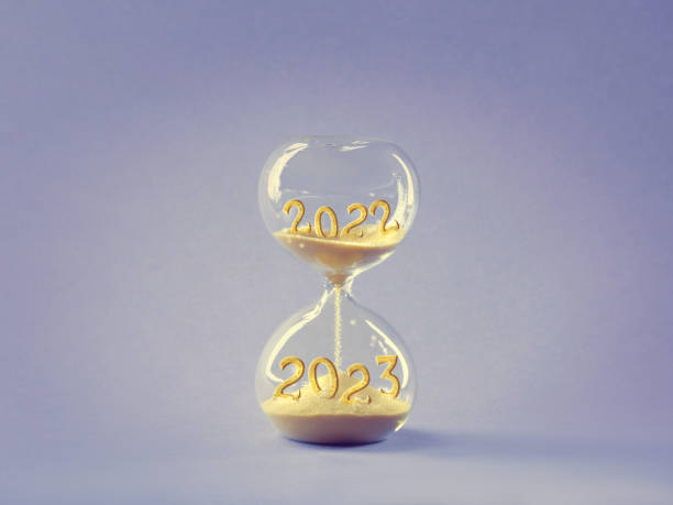 Hourglass, passage of time from 2022 to 2023 year. Wood artistic model hand holding time glass. Countdown to winter holidays. Merry Christmas and a Happy New Year. Light purple golden concept design. stock photo