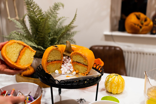 pumpkin-shaped cake with a marshmallow centre surrounded by sweets and treats inside a home on a table.