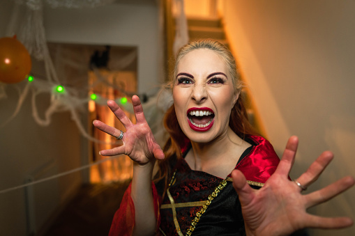 A young adult looking into the camera with her hand up and her mouth open. She is wearing halloween attire in a house.