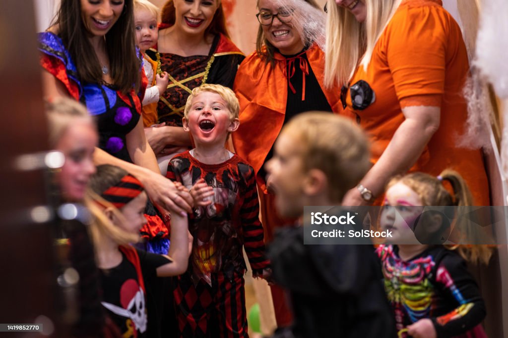 Partying With Friends and Family A group of friends and family with a mixed age range are standing indoors  smiling and talking. They are all dressed up in halloween attire. 12-17 Months Stock Photo