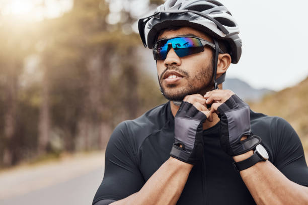 Athletic sportsman wearing glasses and gloves while tying his cycling helmet. Male cyclist putting on a helmet for safety. Professional cyclist getting ready for a ride on a mountain road Athletic sportsman wearing glasses and gloves while tying his cycling helmet. Male cyclist putting on a helmet for safety. Professional cyclist getting ready for a ride on a mountain road professional sportsperson stock pictures, royalty-free photos & images