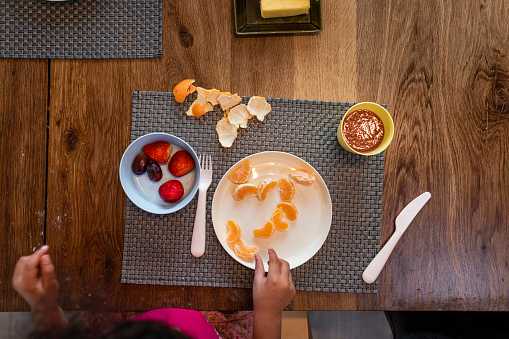 Direct above shot of a young girl sitting at a table eating breakfast in her kitchen in the North East of England. She is eating fruit.