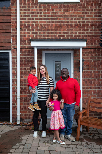 Family with two children standing outside of their home in the North East of England. They are smiling at the camera.