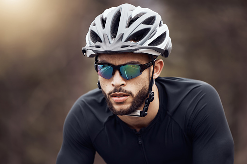 Closeup of one athletic young man cycling outside. Serious guy wearing helmet and glasses while riding a bike for exercise or competition race. Endurance and cardio during a workout and training