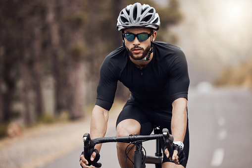 One athletic young man cycling outside. Sporty fit male wearing helmet and glasses while riding a bike on a road along the mountain for exercise. Endurance and cardio during a workout and training