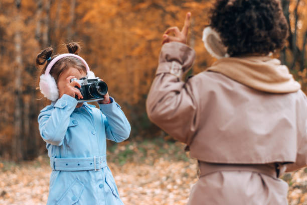 Caucasian and African-American girls take pictures of each other on camera in the autumn park.Technology,diverse people,autumnal concept