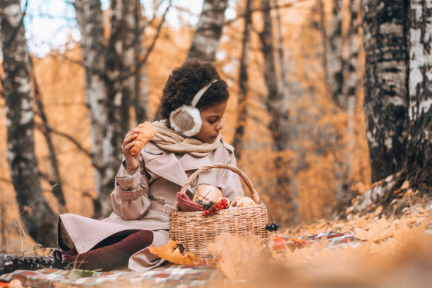 African-American girl eats a croissant at a picnic in an autumn park.Diversity,autumn concept