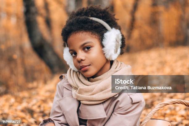 Portrait of a cute African-American girl in fur headphones in an autumn park.Diversity,autumn concept