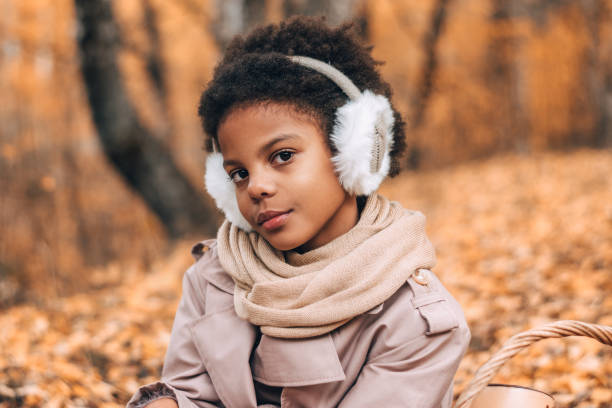 Portrait of a cute African-American girl in fur headphones in an autumn park.Diversity,autumn concept stock photo