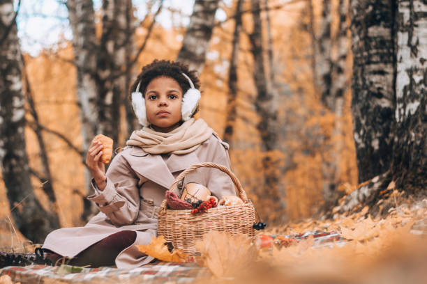 African-American girl eats a croissant at a picnic in an autumn park.Diversity,autumn concept