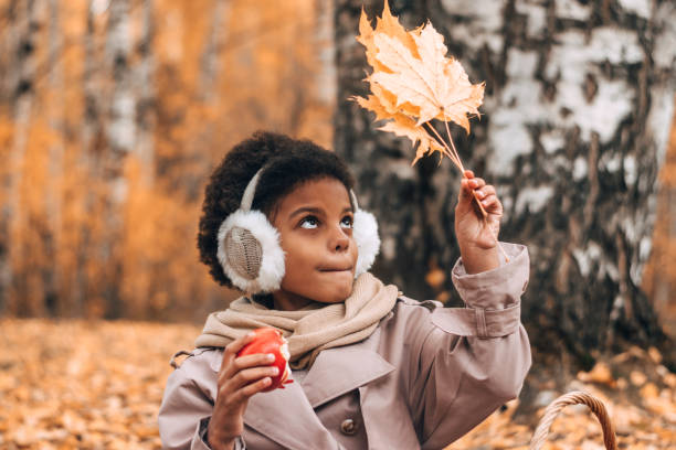 urocza afroamerykańska dziewczyna zjada jabłko i podziwia żółty liść klonu na pikniku w jesiennym parku. różnorodność, jesienna koncepcja - maple leaf audio zdjęcia i obrazy z banku zdjęć