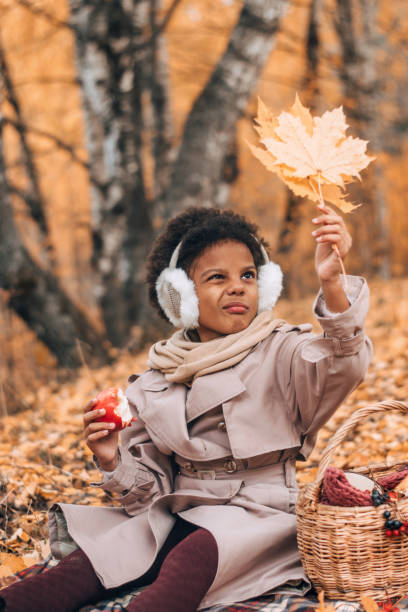 urocza afroamerykańska dziewczyna zjada jabłko i podziwia żółty liść klonu na pikniku w jesiennym parku. różnorodność, jesienna koncepcja - maple leaf audio zdjęcia i obrazy z banku zdjęć