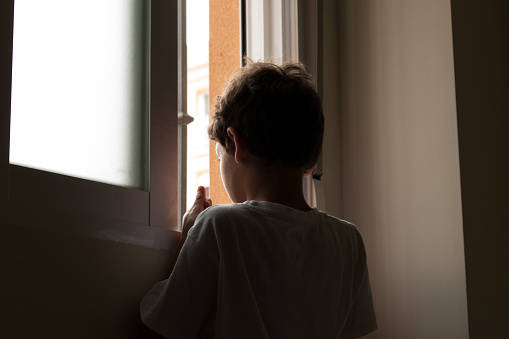 Unrecognizable adolescent looking out window