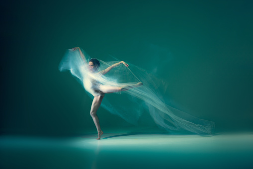 Solo. Beautiful and graceful ballet dancer dancing with white transparent cloth, isolated on cyan color background. Concept of art, motion, action, flexibility and inspiration concept. Blurring effect