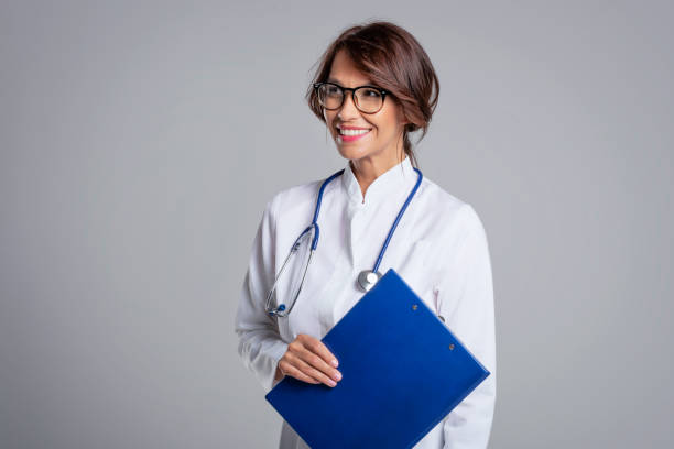 Smiling female doctor standing at isolated grey background and holding clipboard in her hand stock photo
