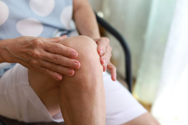 starsza azjatka masująca kolano, cierpiąca na ból nogi podczas siedzenia na krześle w salonie - arthritis senior adult rheumatoid arthritis sadness zdjęcia i obrazy z banku zdjęć