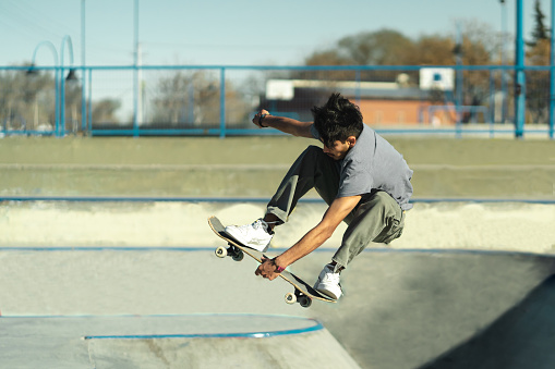 Young skater boy holding his skateboard while jumping in the air on concrete bowl of skatepark