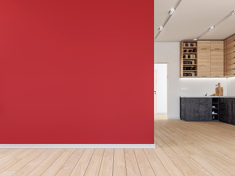 Empty living room with a large red plaster wall background with copy space on the hardwood floor. A modern kitchen in the background with high wooden cabinets and anthracite lower kitchen cabinets on a white plaster wall.  A bright hallway with doors on the side of the kitchen led light reflectors on the ceiling. 3D rendered image.