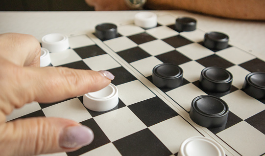 A woman's hand moves a white checker on a black-and-white playing field, the concept of hobbies and home games.