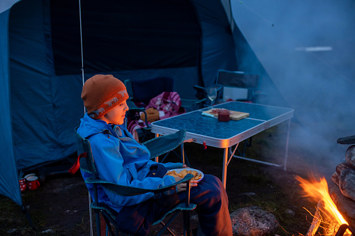 Kids, sitting around campfire at night, enjoying wild camping, family vacation in Norway