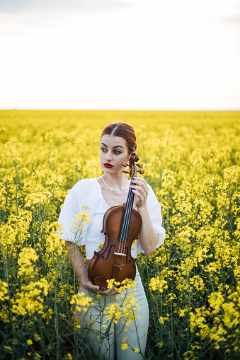 Beautiful ginger hair girl holding violin in field