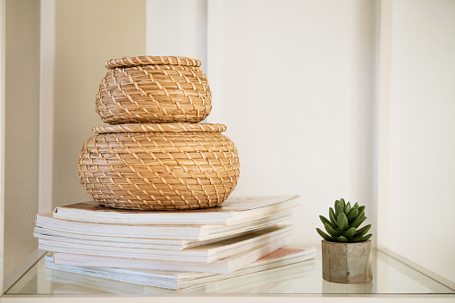 Close-up of a round straw box with a lid on a white shelf. Eco-friendly items for storing small items, organizing space. Home decor decorative items. Stand on a shelf in the room