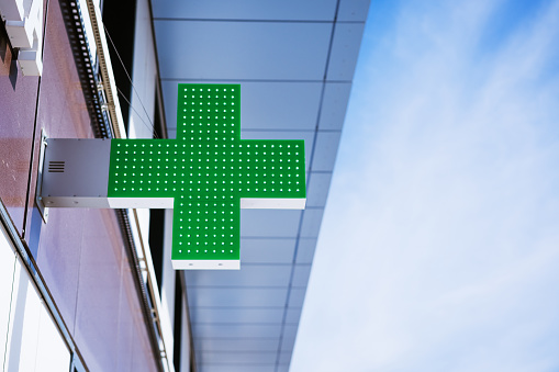 green cross on the facade of a building against a blue sky on a sunny day, medical symbol