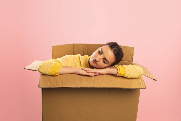 istock Young woman sitting inside open cardboard box with calm and happy expression. Moving into new apartment 1419886595