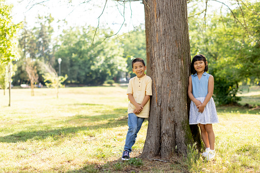 Cute Asian kids posing by the tree in the park